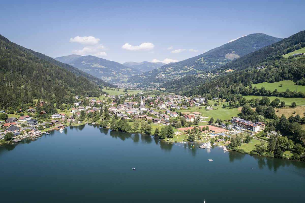 Blick über das kristallklare Wasser des Brennsees auf die Ortschaft Feld am See.