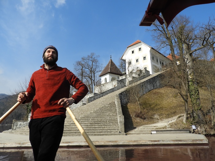 Blaš ist ein erfahrener Pletna-Bootsführer und beherrscht die Technik des Stehruderns perfekt – im Hintergrund die 99 Stufen zur Kirche